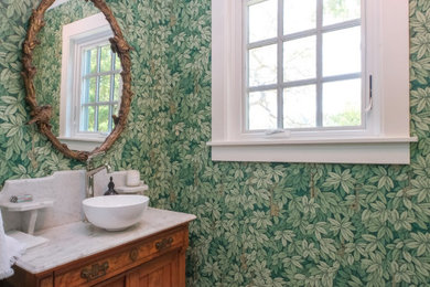 Inspiration for a mid-sized medium tone wood floor, vaulted ceiling and wallpaper powder room remodel in San Francisco with medium tone wood cabinets, a two-piece toilet, green walls, a vessel sink, marble countertops, white countertops and a freestanding vanity