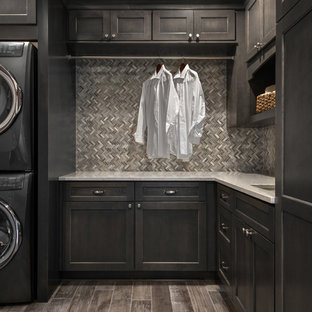 This is an example of a medium sized classic l-shaped utility room in Detroit with a submerged sink, flat-panel cabinets, dark wood cabinets, engineered stone countertops, beige walls, porcelain flooring and a stacked washer and dryer.