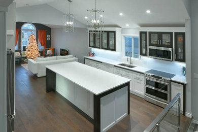 Design ideas for an expansive industrial single-wall open plan kitchen in Other with a double-bowl sink, recessed-panel cabinets, white cabinets, solid surface benchtops, white splashback, subway tile splashback, stainless steel appliances, dark hardwood floors, with island, brown floor, white benchtop and vaulted.
