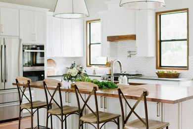 Example of a mid-sized transitional l-shaped medium tone wood floor and brown floor open concept kitchen design in Other with a single-bowl sink, recessed-panel cabinets, white cabinets, wood countertops, gray backsplash, marble backsplash, stainless steel appliances and an island