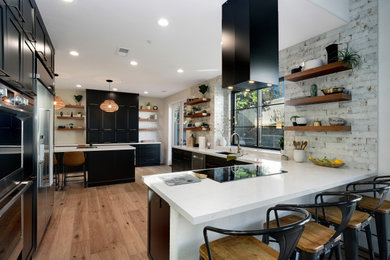 Kitchen - large modern medium tone wood floor and brown floor kitchen idea in San Diego with a single-bowl sink, shaker cabinets, black cabinets, quartz countertops, white backsplash, brick backsplash, stainless steel appliances, an island and white countertops