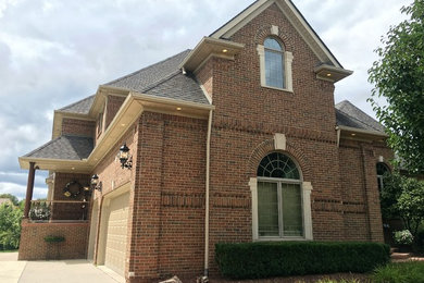 Elegant brown two-story brick house exterior photo in Detroit with a hip roof and a shingle roof