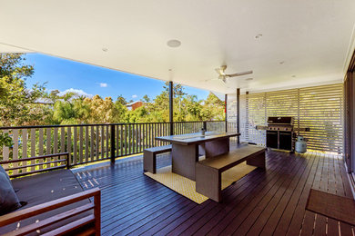 This is an example of a large contemporary balcony in Brisbane with a roof extension and wood railing.