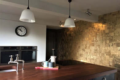 Inspiration for a large rural u-shaped kitchen/diner in London with a submerged sink, flat-panel cabinets, black cabinets, wood worktops, integrated appliances, medium hardwood flooring and an island.