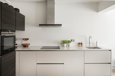 This is an example of a contemporary l-shaped open plan kitchen in London with a single-bowl sink, flat-panel cabinets, solid surface benchtops and stainless steel appliances.