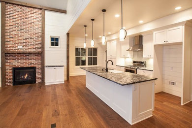 Example of a mid-sized classic single-wall dark wood floor and brown floor open concept kitchen design in Denver with a farmhouse sink, shaker cabinets, white cabinets, gray backsplash, glass tile backsplash, stainless steel appliances and an island