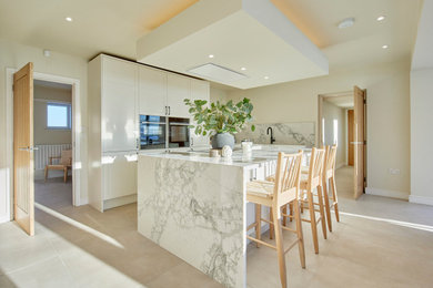 Inspiration for a large modern grey and white l-shaped kitchen/diner in Other with a built-in sink, shaker cabinets, white cabinets, quartz worktops, white splashback, engineered quartz splashback, integrated appliances, an island, beige floors and white worktops.