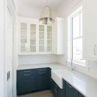 Photo of a large beach style l-shaped kitchen pantry in Charleston with a farmhouse sink, shaker cabinets, blue cabinets, quartz benchtops, white splashback, porcelain splashback, coloured appliances, medium hardwood floors, with island, brown floor and white benchtop.