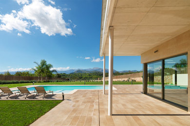 Diseño de piscina alargada actual grande en forma de L en patio trasero con privacidad y suelo de baldosas
