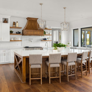 Ejemplo de cocina en U, campestre, extra grande, con fregadero sobremueble, armarios estilo shaker, puertas de armario blancas, salpicadero blanco, salpicadero de losas de piedra, electrodomésticos de acero inoxidable, una isla, suelo marrón, encimeras blancas, encimera de cuarzo compacto y suelo de madera en tonos medios