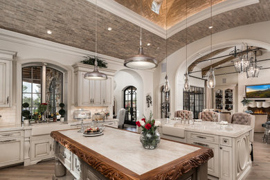 Example of a huge transitional u-shaped brown floor, dark wood floor and vaulted ceiling enclosed kitchen design in Phoenix with a farmhouse sink, raised-panel cabinets, light wood cabinets, quartzite countertops, two islands, multicolored backsplash, porcelain backsplash, beige countertops and paneled appliances