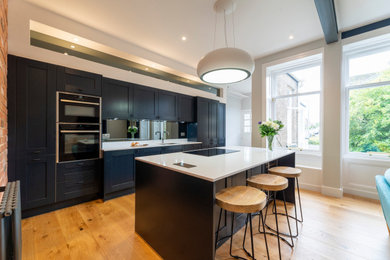 Photo of a large traditional single-wall open plan kitchen in Edinburgh with an integrated sink, shaker cabinets, blue cabinets, quartz worktops, black splashback, mirror splashback, stainless steel appliances, light hardwood flooring, an island, orange floors and white worktops.