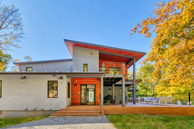 Mid-sized gray two-story stucco house exterior photo in New York with a shed roof, a metal roof and a black roof