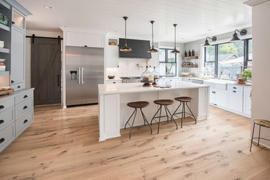 Kitchen - large country u-shaped light wood floor and beige floor kitchen idea in Seattle with a farmhouse sink, white cabinets, marble countertops, white backsplash, ceramic backsplash, stainless steel appliances, an island, white countertops and shaker cabinets