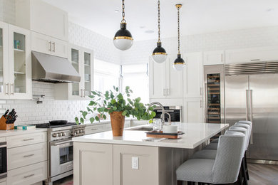Kitchen - transitional l-shaped dark wood floor and brown floor kitchen idea in Los Angeles with an undermount sink, white cabinets, white backsplash, subway tile backsplash, stainless steel appliances, an island, white countertops and glass-front cabinets