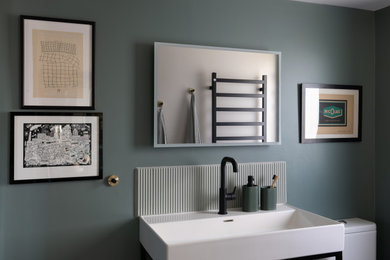 Small contemporary ensuite bathroom in London with flat-panel cabinets, medium wood cabinets, an alcove shower, a one-piece toilet, green tiles, ceramic tiles, green walls, ceramic flooring, a console sink, grey floors, a hinged door, a wall niche, a single sink and a freestanding vanity unit.