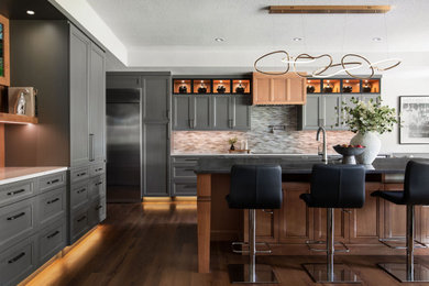 Kitchen - huge transitional l-shaped medium tone wood floor and brown floor kitchen idea in Austin with an undermount sink, recessed-panel cabinets, gray cabinets, mosaic tile backsplash, stainless steel appliances, an island, white countertops and gray backsplash