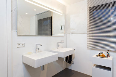 Exempel på ett mellanstort modernt en-suite badrum, med vita skåp, ett fristående badkar, en vägghängd toalettstol, vit kakel, stenkakel, vita väggar, ett väggmonterat handfat, bänkskiva i akrylsten och grått golv