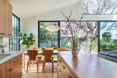 Example of a mid-sized 1950s galley medium tone wood floor, brown floor and vaulted ceiling open concept kitchen design in Los Angeles with an undermount sink, flat-panel cabinets, brown cabinets, wood countertops, green backsplash, ceramic backsplash, paneled appliances, an island and brown countertops