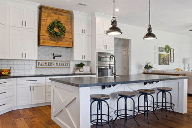 Example of a large l-shaped medium tone wood floor and brown floor open concept kitchen design in Phoenix with a farmhouse sink, shaker cabinets, white cabinets, concrete countertops, white backsplash, subway tile backsplash, stainless steel appliances, an island and gray countertops