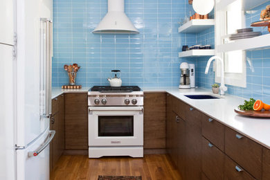 Example of a 1960s u-shaped medium tone wood floor kitchen design in Atlanta with an undermount sink, flat-panel cabinets, dark wood cabinets, blue backsplash, white appliances, no island and white countertops