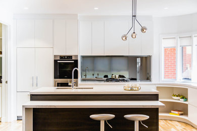This is an example of a mid-sized contemporary l-shaped open plan kitchen in Melbourne with an undermount sink, flat-panel cabinets, dark wood cabinets, quartz benchtops, metallic splashback, mirror splashback, stainless steel appliances, light hardwood floors, with island, yellow floor and multi-coloured benchtop.