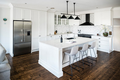 Photo of a transitional l-shaped open plan kitchen in Melbourne with an undermount sink, shaker cabinets, white cabinets, white splashback, subway tile splashback, stainless steel appliances, dark hardwood floors, with island, brown floor and white benchtop.