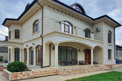 Стильный дизайн: большой, двухэтажный, бежевый дом в классическом стиле с комбинированной облицовкой, вальмовой крышей, крышей из гибкой черепицы и коричневой крышей - последний тренд