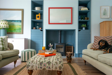 Medium sized classic enclosed living room in Gloucestershire with blue walls, light hardwood flooring, a wood burning stove, a timber clad chimney breast, no tv and tongue and groove walls.