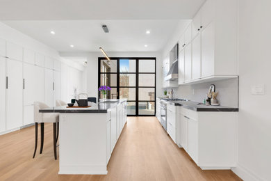 Inspiration for a huge modern galley medium tone wood floor kitchen pantry remodel in New York with an undermount sink, beaded inset cabinets, white cabinets, marble countertops, white backsplash, marble backsplash, paneled appliances, an island and black countertops