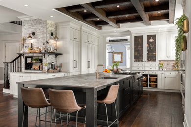 Large mountain style dark wood floor, brown floor and wood ceiling eat-in kitchen photo in Tampa with a farmhouse sink, recessed-panel cabinets, gray backsplash, ceramic backsplash, paneled appliances and an island