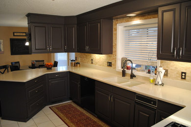 Example of a large transitional ceramic tile eat-in kitchen design in New York with an undermount sink, brown cabinets, solid surface countertops, beige backsplash, stone tile backsplash, black appliances and a peninsula