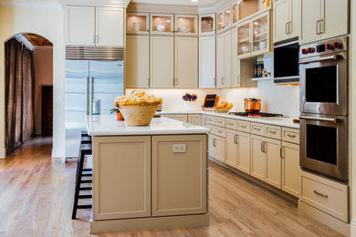 Photo of a mid-sized traditional l-shaped eat-in kitchen in San Francisco with a single-bowl sink, recessed-panel cabinets, beige cabinets, marble benchtops, beige splashback, porcelain splashback, stainless steel appliances, light hardwood floors, with island and beige floor.