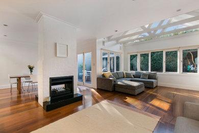 Example of a large brown floor family room design with white walls and a two-sided fireplace