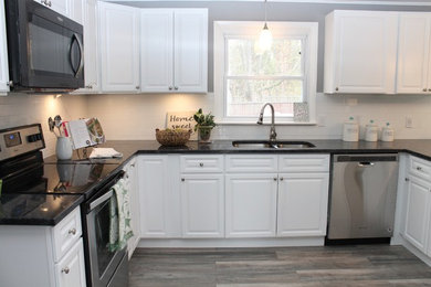Mid-sized beach style u-shaped eat-in kitchen photo in New York with raised-panel cabinets, white cabinets, white backsplash, ceramic backsplash, stainless steel appliances, a peninsula and black countertops