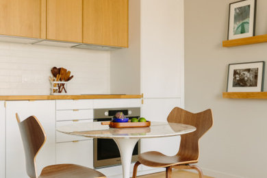 Cette image montre une cuisine américaine linéaire, bicolore et blanche et bois minimaliste de taille moyenne avec un plan de travail en bois, une crédence blanche, une crédence en carrelage métro et parquet clair.