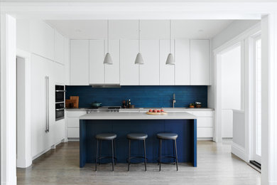 Ejemplo de cocinas en L minimalista con armarios con paneles lisos, puertas de armario blancas, salpicadero azul, una isla y encimeras grises