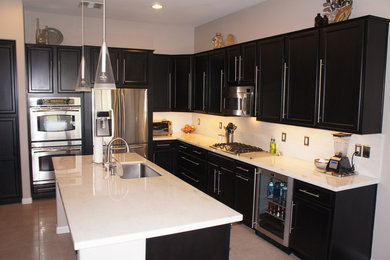 Example of a trendy l-shaped ceramic tile eat-in kitchen design in Phoenix with a drop-in sink, recessed-panel cabinets, black cabinets, marble countertops, white backsplash, stone slab backsplash, stainless steel appliances and an island