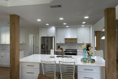 Example of a single-wall vinyl floor and brown floor kitchen pantry design in Other with an undermount sink, shaker cabinets, white cabinets, quartz countertops, beige backsplash, marble backsplash, stainless steel appliances, an island and white countertops