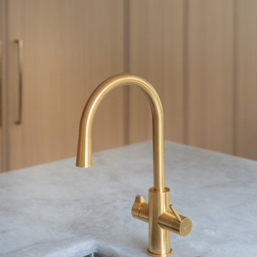 An elegant and modern kitchen faucet with a gold finish, placed near a large win