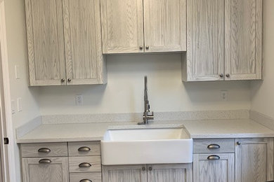 Example of a mid-sized beach style single-wall vinyl floor and beige floor utility room design in Other with a farmhouse sink, recessed-panel cabinets, white cabinets, solid surface countertops, white walls, a side-by-side washer/dryer and white countertops