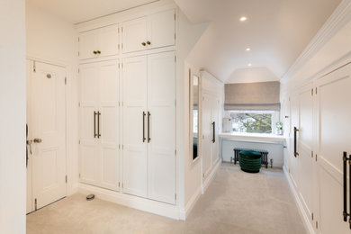 Large modern gender neutral built-in wardrobe in Essex with shaker cabinets, white cabinets, carpet and beige floors.