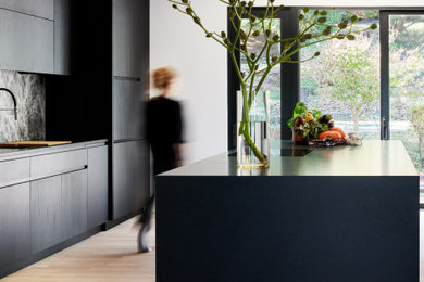 Trendy light wood floor kitchen photo in New York with an undermount sink, flat-panel cabinets, black cabinets, granite countertops, multicolored backsplash, marble backsplash, black appliances, an island and black countertops