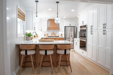 Mid-sized country u-shaped light wood floor and brown floor eat-in kitchen photo in Nashville with an undermount sink, shaker cabinets, white cabinets, quartzite countertops, white backsplash, marble backsplash, stainless steel appliances, an island and white countertops
