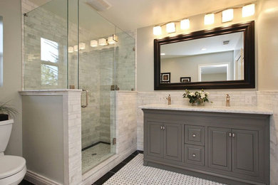 Example of a mid-sized transitional 3/4 gray tile and porcelain tile ceramic tile and white floor corner shower design in Orange County with raised-panel cabinets, gray cabinets, a two-piece toilet, gray walls, an undermount sink, marble countertops and a hinged shower door