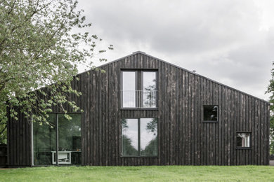 This is an example of a large and black farmhouse two floor detached house in Hertfordshire with wood cladding, a pitched roof, a metal roof, a grey roof and board and batten cladding.