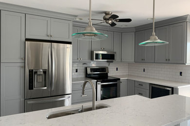 Inspiration for a mid-sized transitional l-shaped porcelain tile and white floor open concept kitchen remodel in Miami with an undermount sink, flat-panel cabinets, gray cabinets, quartz countertops, white backsplash, ceramic backsplash, stainless steel appliances, a peninsula and white countertops