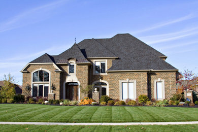 Large elegant brown two-story brick house exterior photo in Raleigh with a hip roof, a shingle roof and a black roof