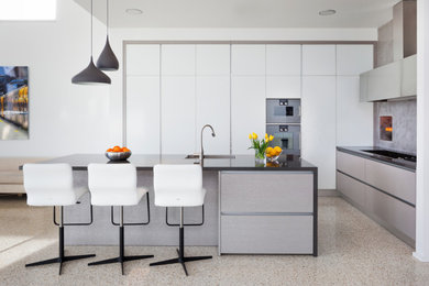 Large industrial l-shaped eat-in kitchen in Perth with an integrated sink, flat-panel cabinets, solid surface benchtops, grey splashback, mosaic tile splashback, stainless steel appliances, terrazzo floors, with island, beige floor and black benchtop.