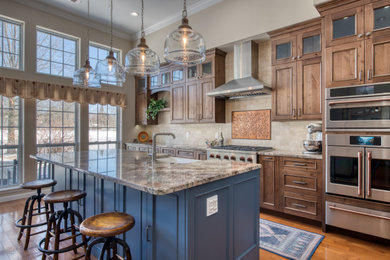 Mid-sized transitional single-wall medium tone wood floor and brown floor kitchen photo in New York with a farmhouse sink, recessed-panel cabinets, distressed cabinets, granite countertops, beige backsplash, marble backsplash, stainless steel appliances, an island and multicolored countertops